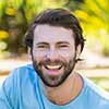 Smiling man outdoors with a beard and casual blue shirt.
