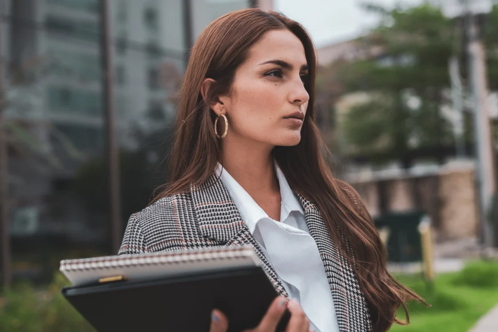 Confident woman in a blazer holding a notebook outdoors.